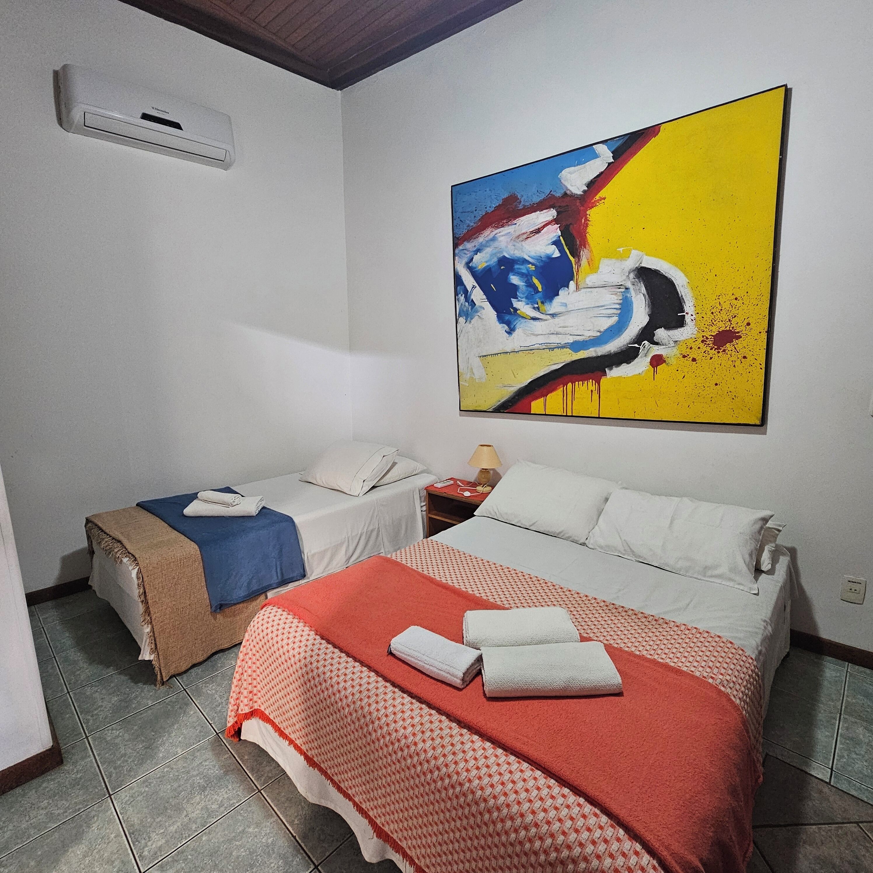 A hotel room with two beds, a large abstract painting on the wall, and an air conditioning unit.