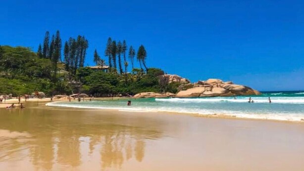 Una playa con agua azul cristalina, orilla arenosa y afloramientos rocosos.