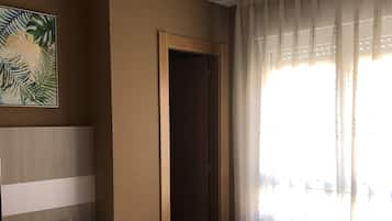Een slaapkamer met een bed, een plafondventilator, een nachtkastje, een telefoon, een deur en een raam met gordijnen.