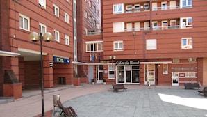 A hotel with a red brick facade, multiple balconies, and a central courtyard with benches. - Hotel Bahía (Gijon)