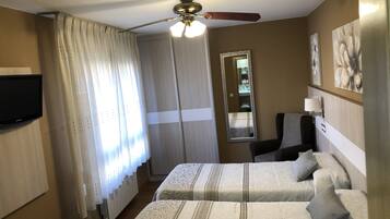 Habitación de hotel con dos camas, ventilador de techo, televisor, espejo y obras de arte en la pared.