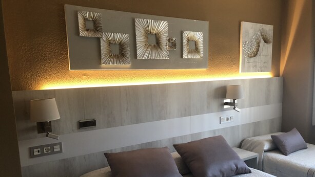 A hotel room with two beds, a wooden headboard, wall-mounted artwork, bedside lamps, and a power outlet. - Hotel Bahía (Gijon)