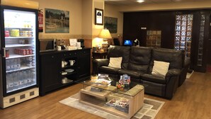 A hotel lobby with a refrigerator stocked with beverages, a coffee machine, a leather sofa, a glass coffee table, and a computer on a desk. - Hotel Bahía (Gijon)