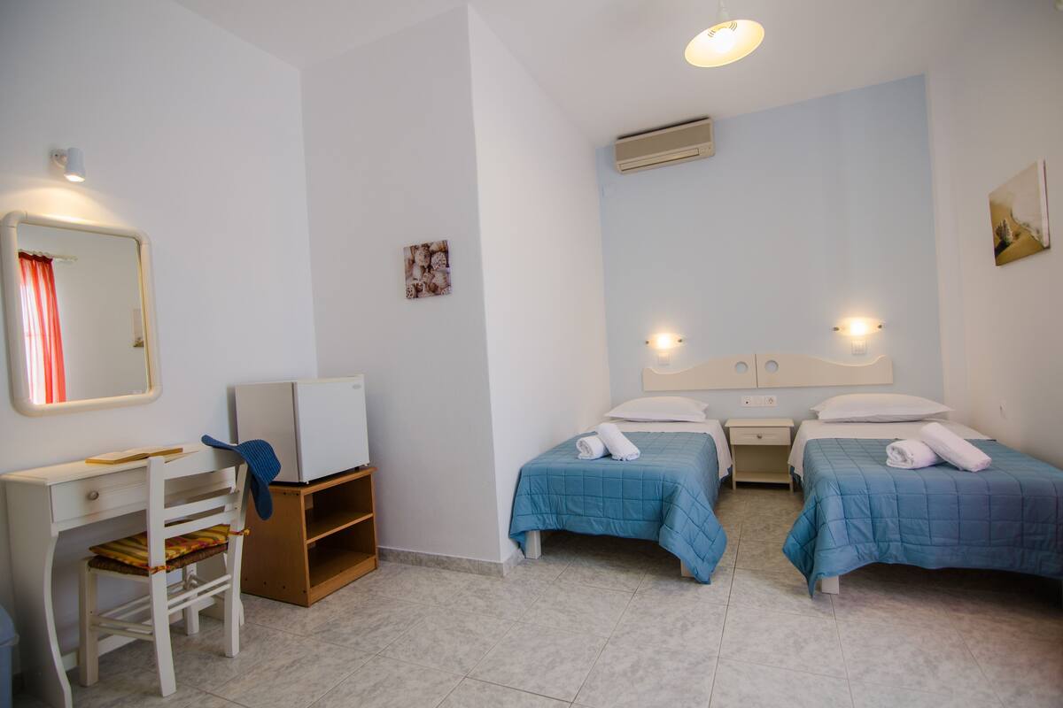 A hotel room with two beds, a desk, a chair, and a TV.