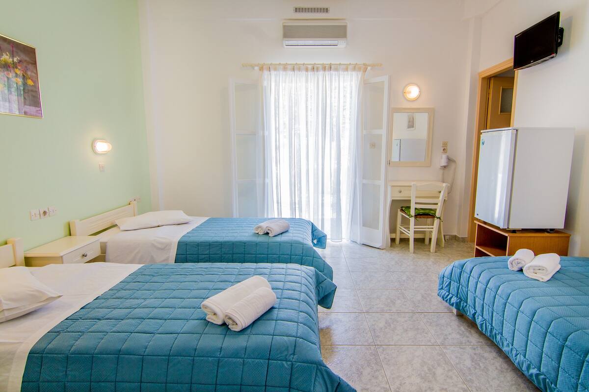 A hotel room with two beds, a desk, a chair, a TV, and a refrigerator.
