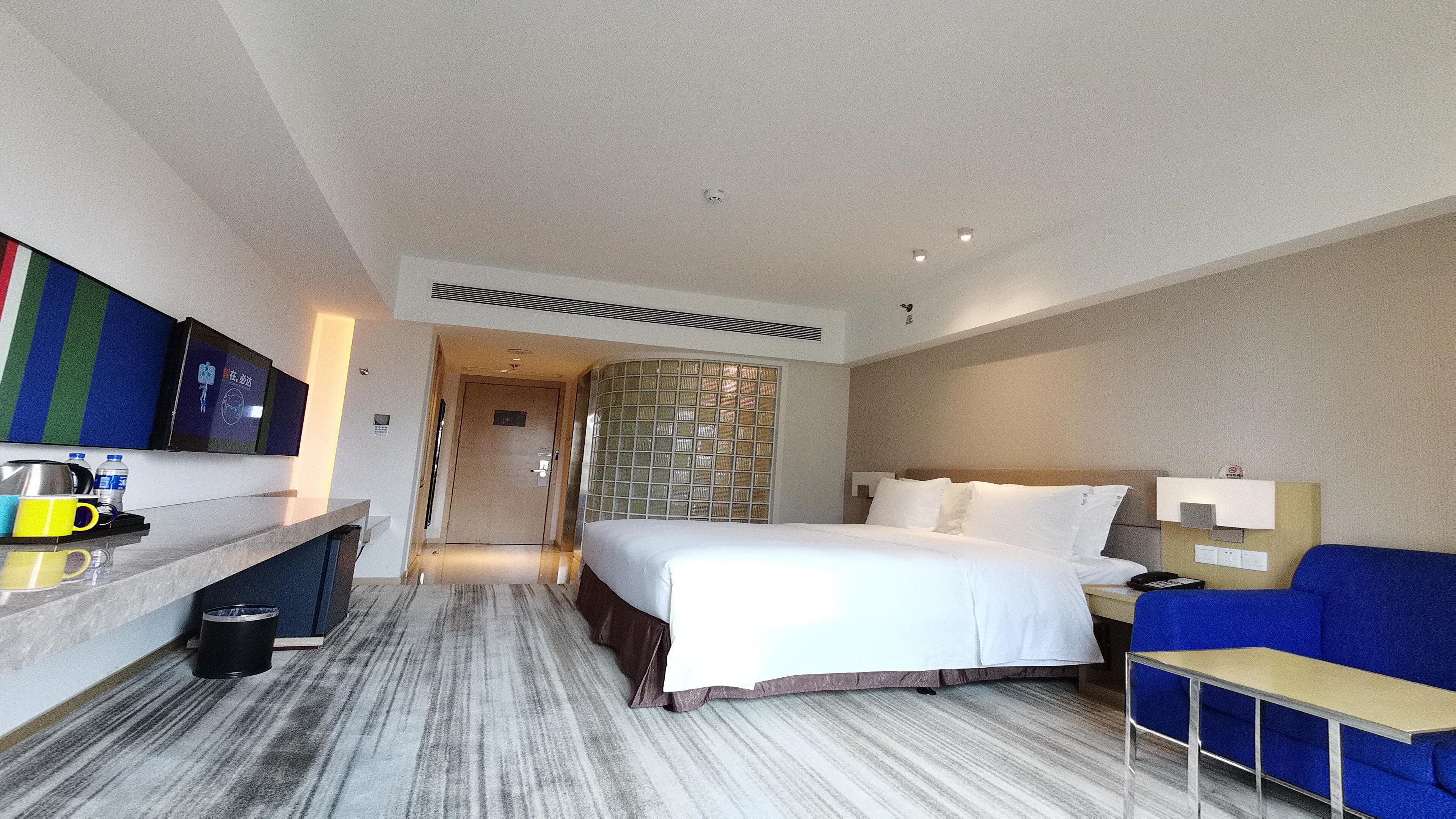 Quarto de hotel com cama, escrivaninha, cadeira, televisão e banheiro.