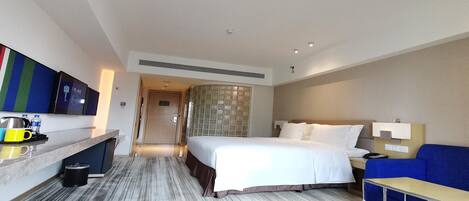A hotel room with a bed, a desk, a chair, a TV, and a bathroom.