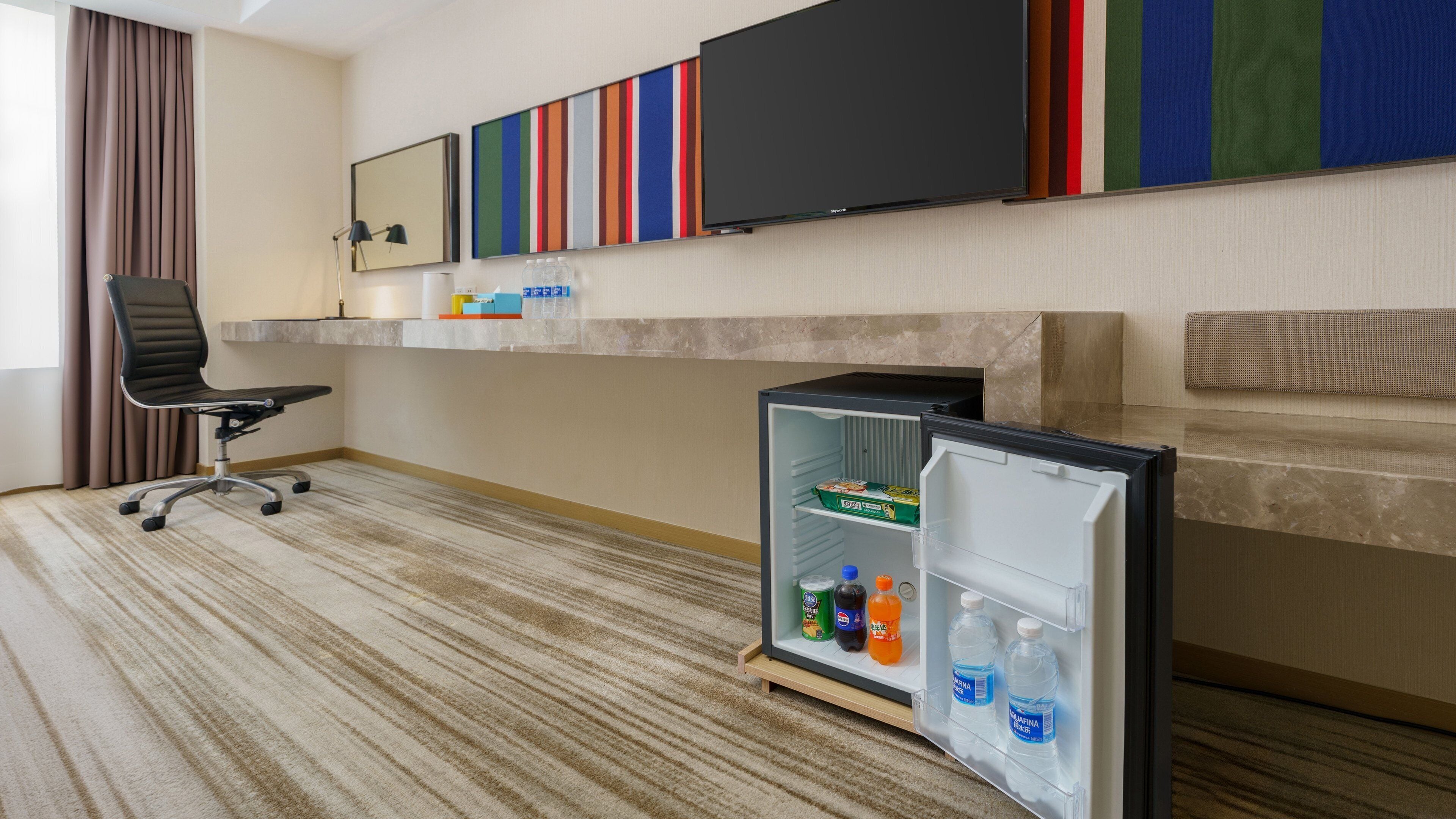 Une chambre d’hôtel dotée d’un téléviseur à écran plat fixé au-dessus d’un mini-bar, d’un bureau avec une chaise et d’un sol recouvert de moquette.