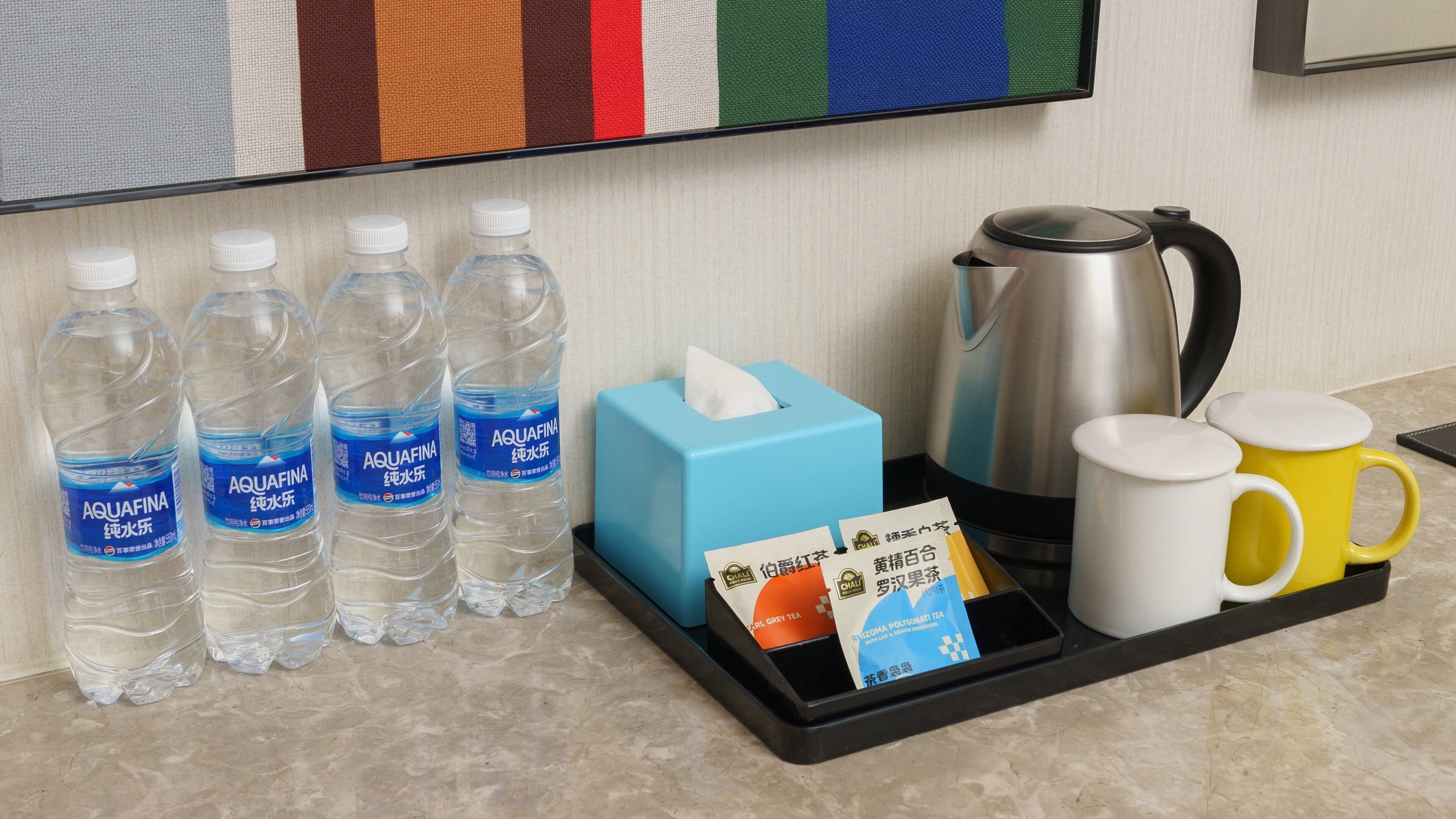 De minibar in een hotelkamer, met waterflesjes, zakdoekjes, een theeservies en een waterkoker.