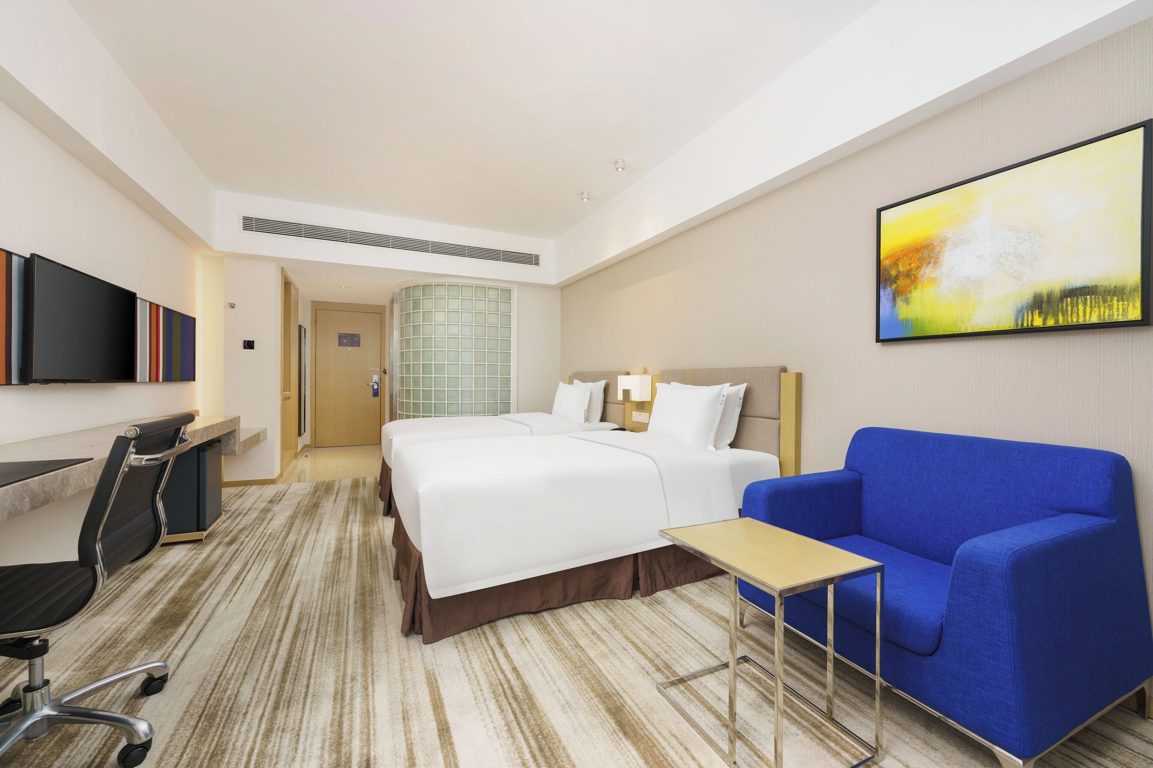 Une chambre d’hôtel avec un lit, un bureau, une chaise, un canapé bleu et un tableau au mur.