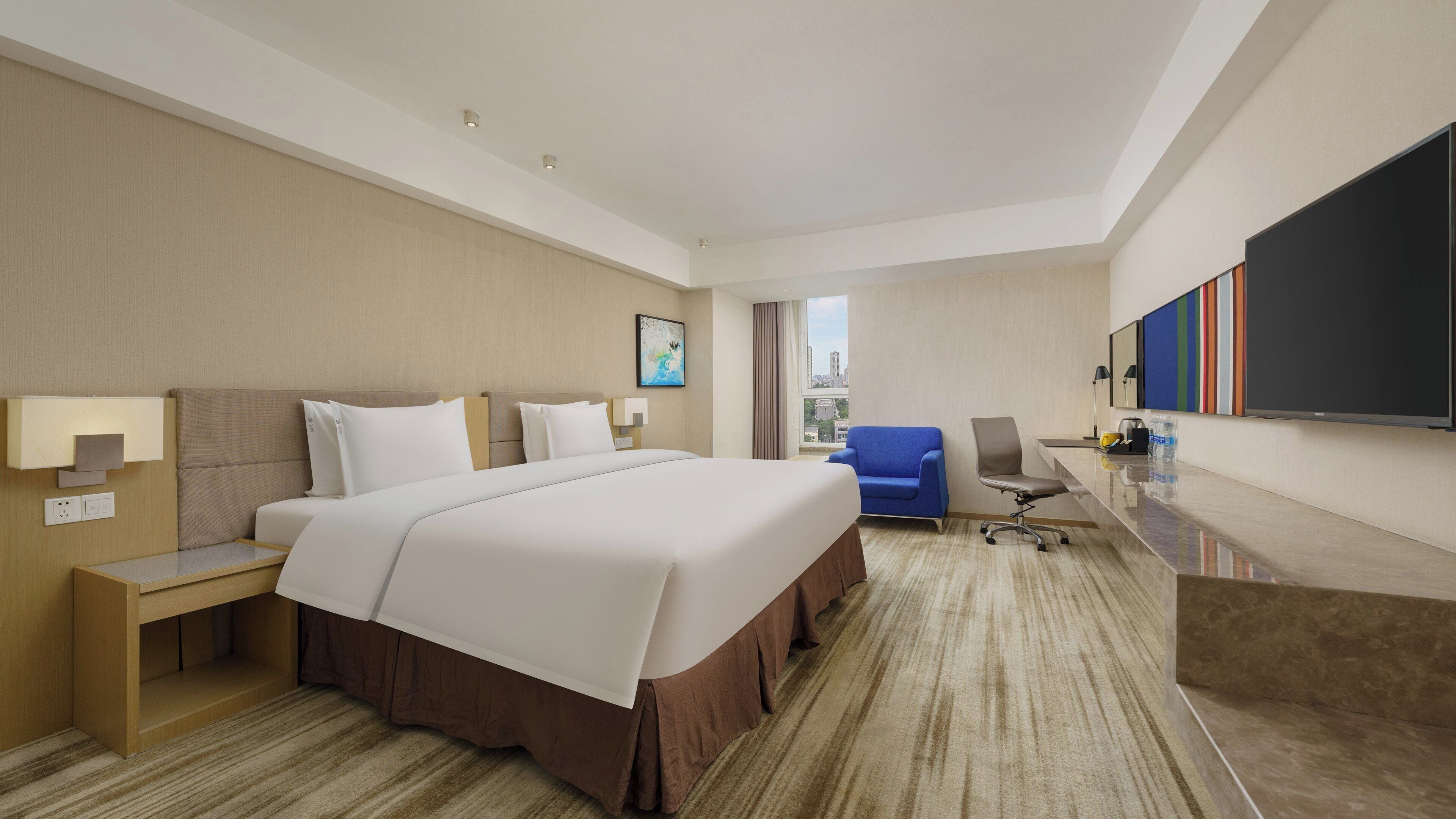 A hotel room with a large bed, a desk, a chair, and a flat-screen TV.