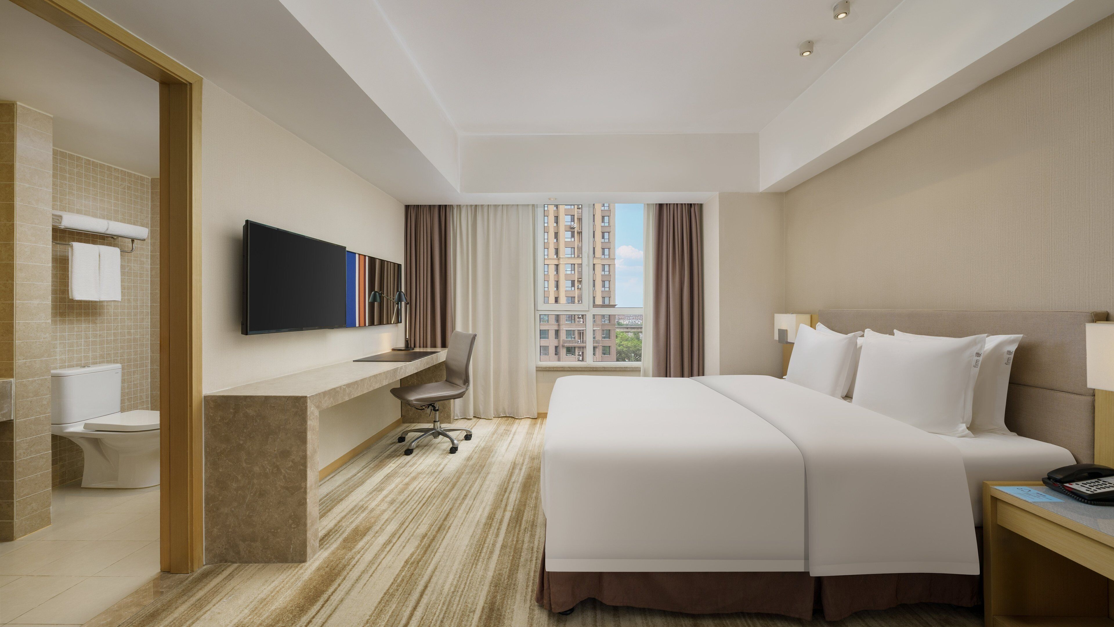 A hotel room with a bed, desk, chair, and a TV on the wall.