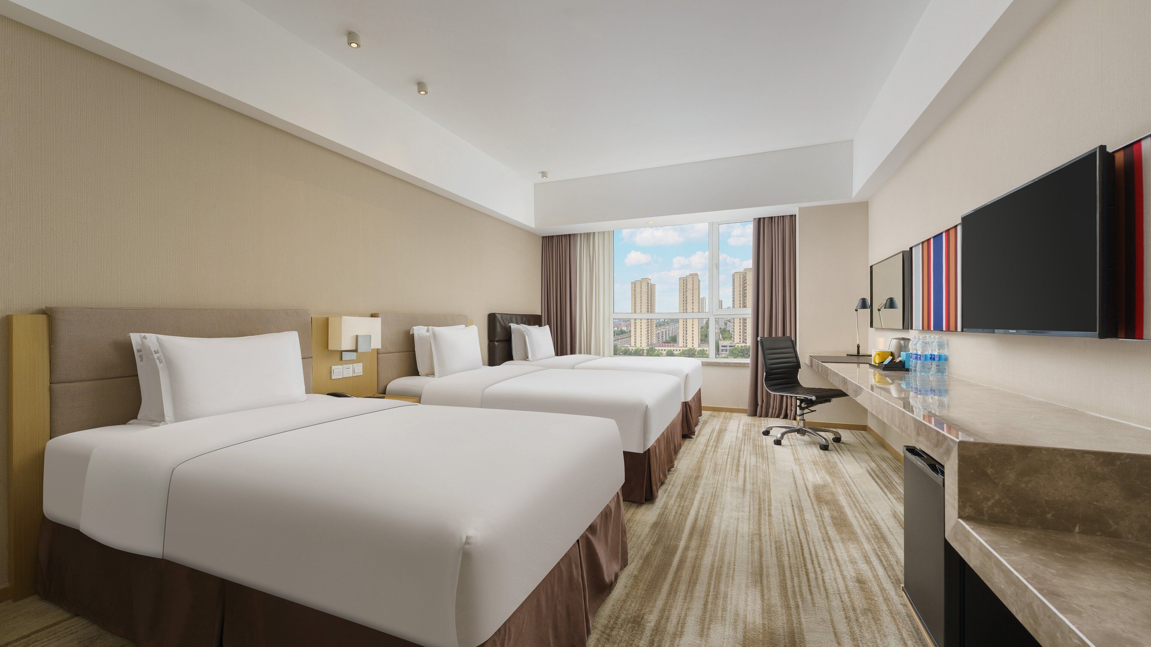 Une chambre d’hôtel avec deux lits, un bureau, une chaise, une grande fenêtre donnant sur la ville et un téléviseur à écran plat.
