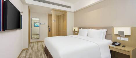 A hotel room with a large bed, bedside table with a lamp, a TV mounted on the wall, and a mirror.