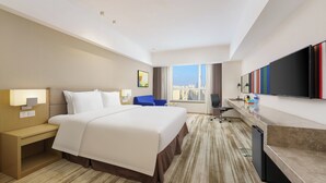 Habitación de hotel con una cama grande, un escritorio, una silla, un televisor y una ventana con vistas a la ciudad.