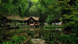 A rustic wooden structure with a thatched roof, surrounded by lush greenery and a pond. - Holiday Inn Chengdu Qinhuang by IHG (Chengdu)