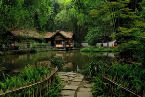 A rustic wooden structure with a thatched roof, surrounded by lush greenery and a pond. - Holiday Inn Chengdu Qinhuang by IHG (Chengdu)