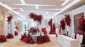 A reception area with a white reception desk, red floral decorations, and a modern ceiling design.