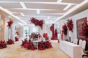 Un espace d’accueil doté d’un comptoir de réception blanc, de décorations florales rouges et d’un design de plafond moderne.