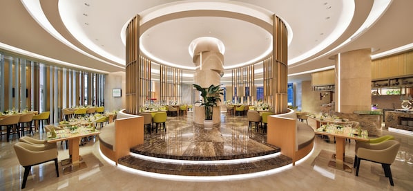 Un moderno vestíbulo de hotel con una escalera central, zona de comedor y una cocina al fondo.