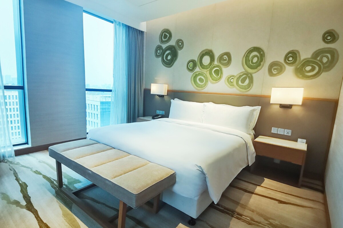 A modern hotel room with a large bed, bedside tables, and a view of the city.