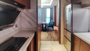 A modern kitchen with a built-in stove, a refrigerator, and a dining area with a table and chairs. - Holiday Inn Chengdu Qinhuang by IHG (Chengdu)
