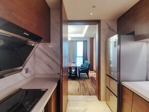 A modern kitchen with a built-in stove, a refrigerator, and a dining area with a table and chairs. - Holiday Inn Chengdu Qinhuang by IHG (Chengdu)