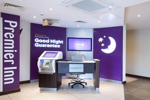 Zona de recepción en Premier Inn con un quiosco de autoservicio, un monitor de computadora y un escritorio con un letrero que dice 'Check In'.