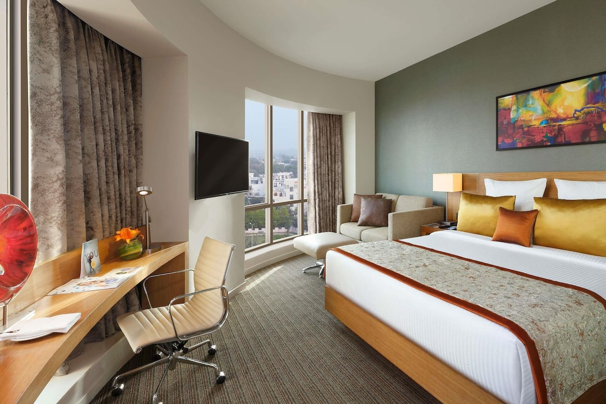 A hotel room with a bed, desk, chair, TV, and a city view.