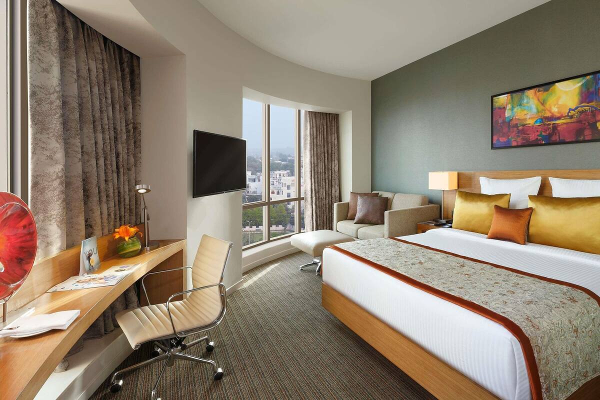 A hotel room with a bed, desk, chair, TV, and a city view.