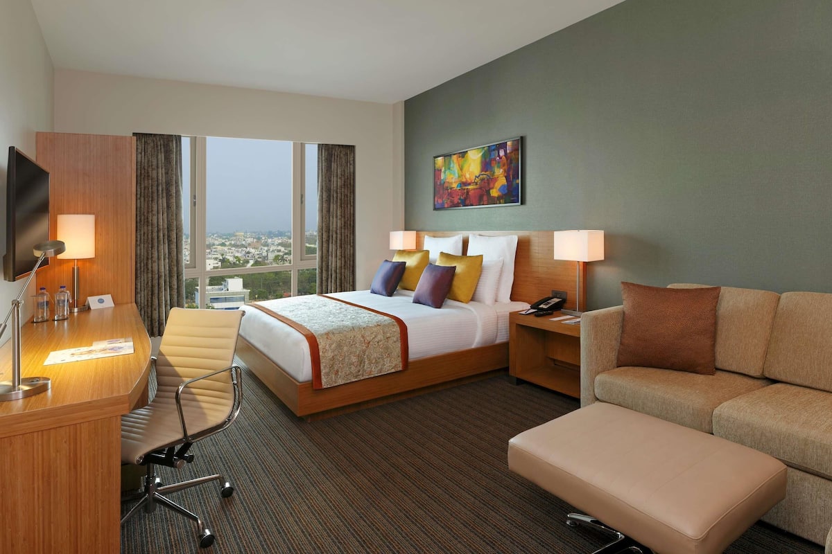 Una habitación de hotel con cama, escritorio, silla, sofá y televisor.