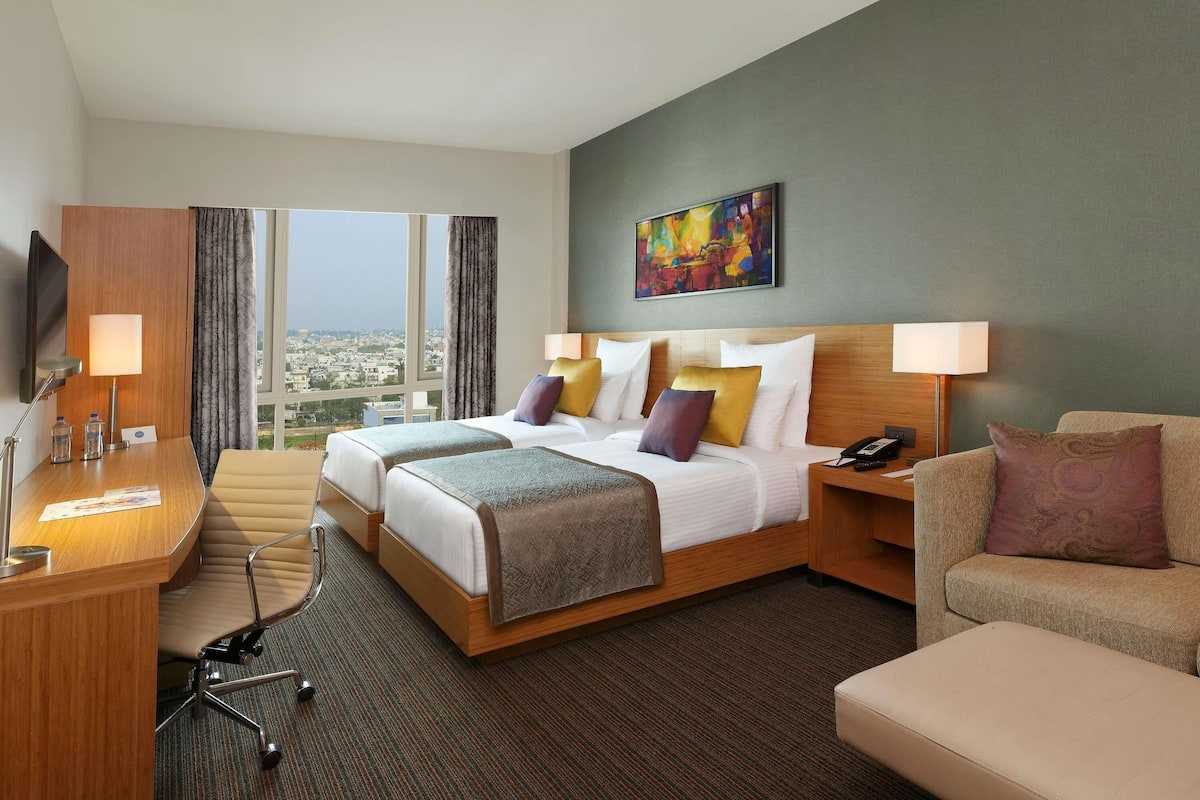 A hotel room with a large bed, two bedside tables, a desk, a chair, a sofa, and a TV.