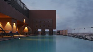 Piscina infinita en la azotea con sillones de descanso y vistas a la ciudad.