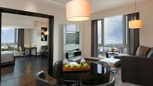 Una habitación de hotel moderna con comedor, sofá, televisor y vistas a la ciudad.