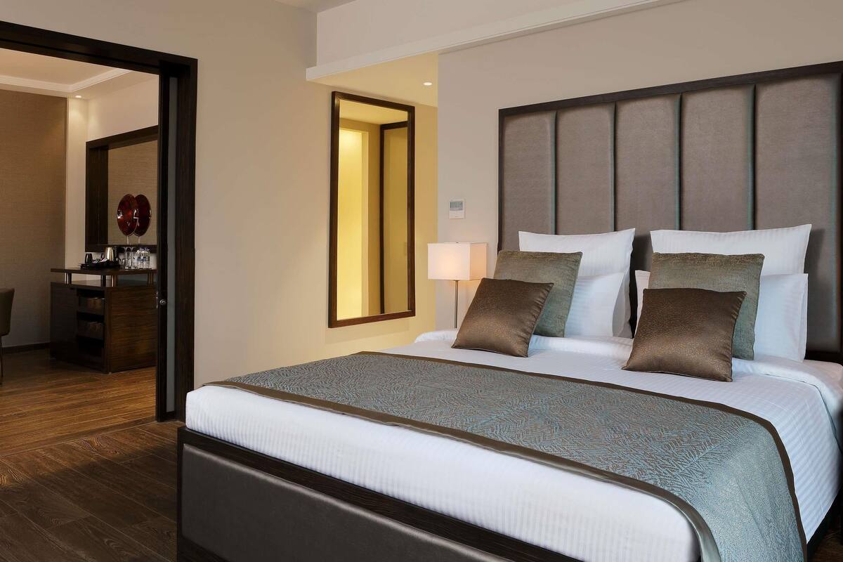 A hotel room with a large bed, a bedside table, a mirror, and a door leading to a bathroom.