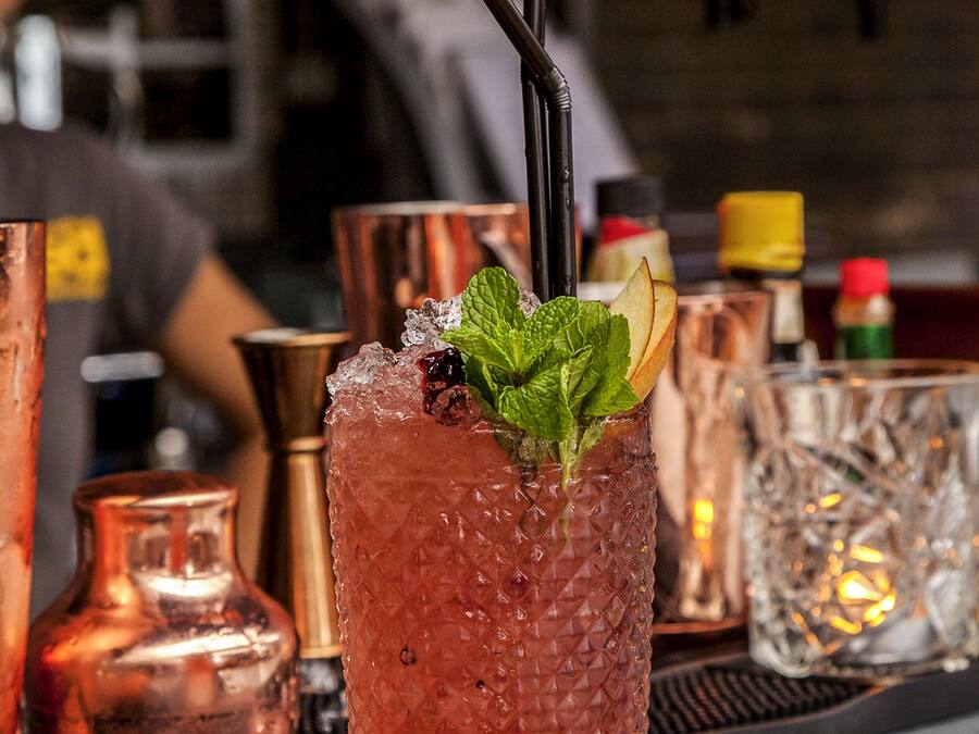 A cocktail glass with a mint garnish and a straw, placed on a bar mat.