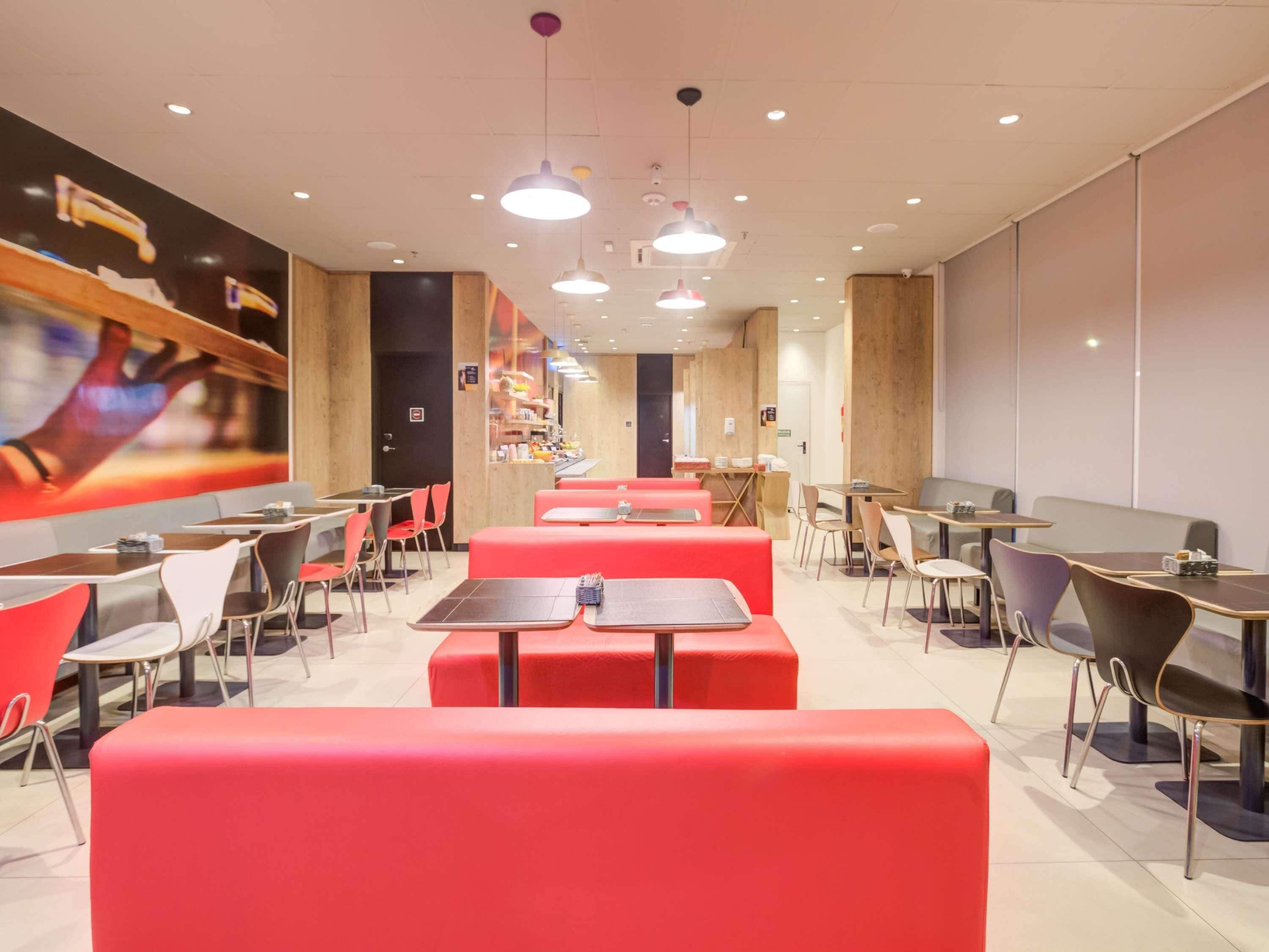 A modern restaurant with red booths and tables, wooden accents, and pendant lighting.