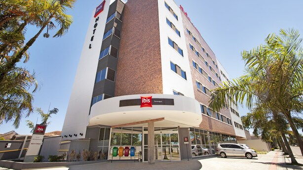Un hotel moderno con un llamativo letrero de 'ibis', una entrada cubierta y un área de estacionamiento.