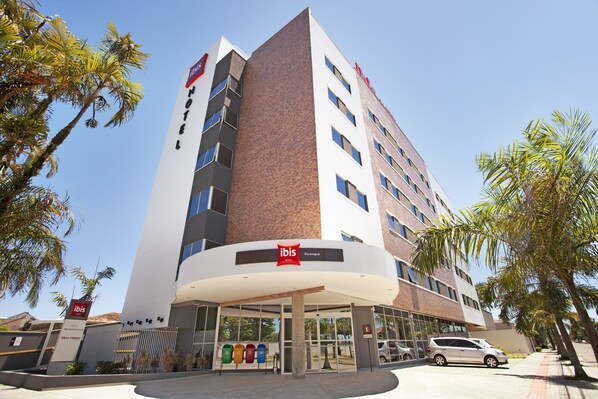 A modern hotel with a prominent 'ibis' sign, a covered entrance, and a parking area. - Ibis Paranagua (Paranaguá)