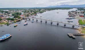 A river with a bridge connecting two land masses, boats, and a cityscape with buildings and greenery. - Ibis Paranagua (Paranaguá)