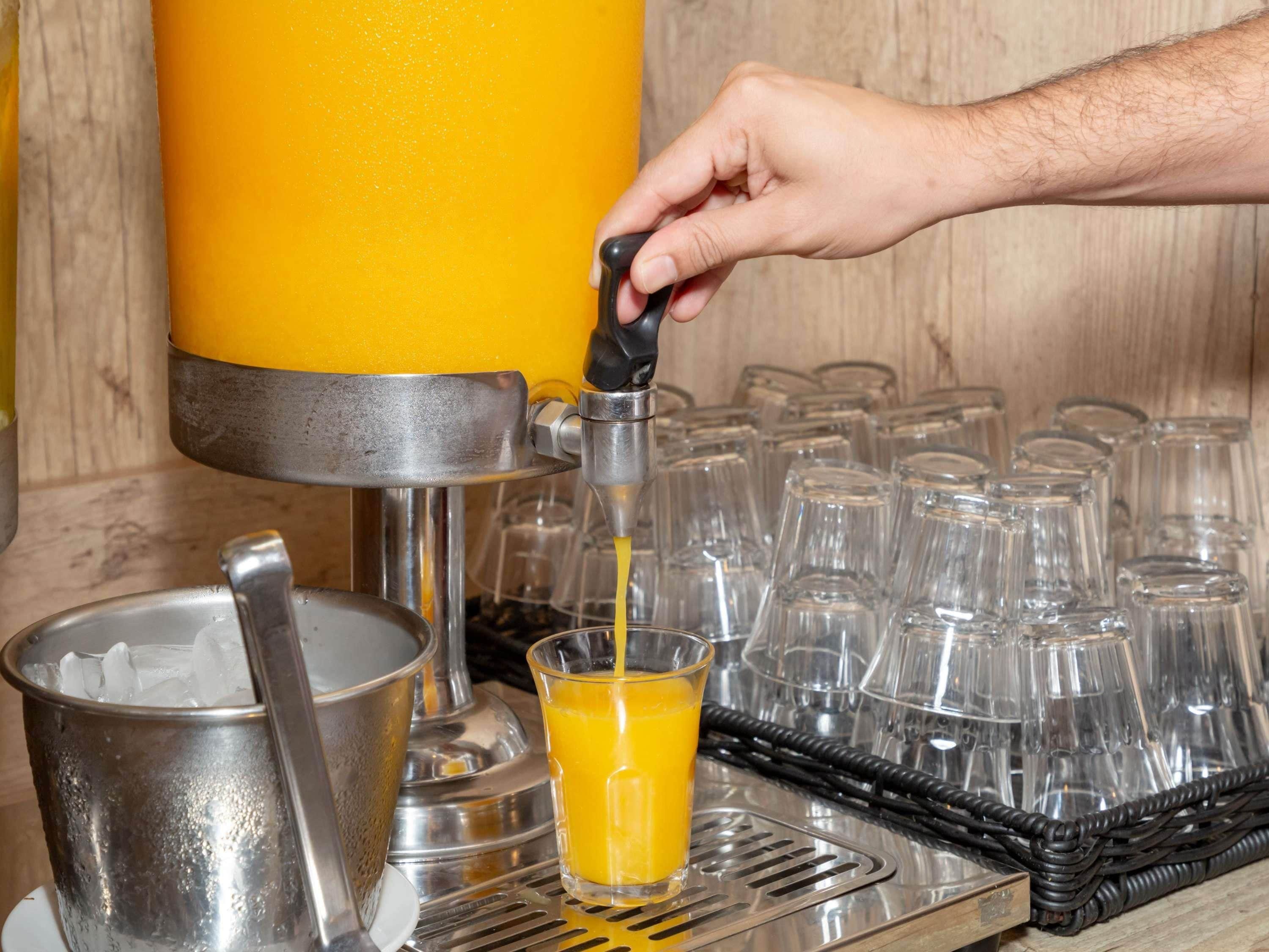 Una mano exprimiendo jugo de naranja de un dispensador en un vaso.