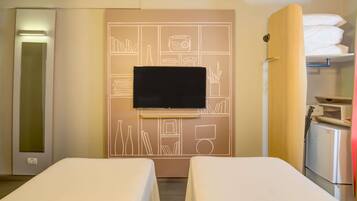 Hotelkamer met twee bedden, een flatscreen-tv aan een wand met een geometrisch patroon, een kledingkast en een kitchenette.