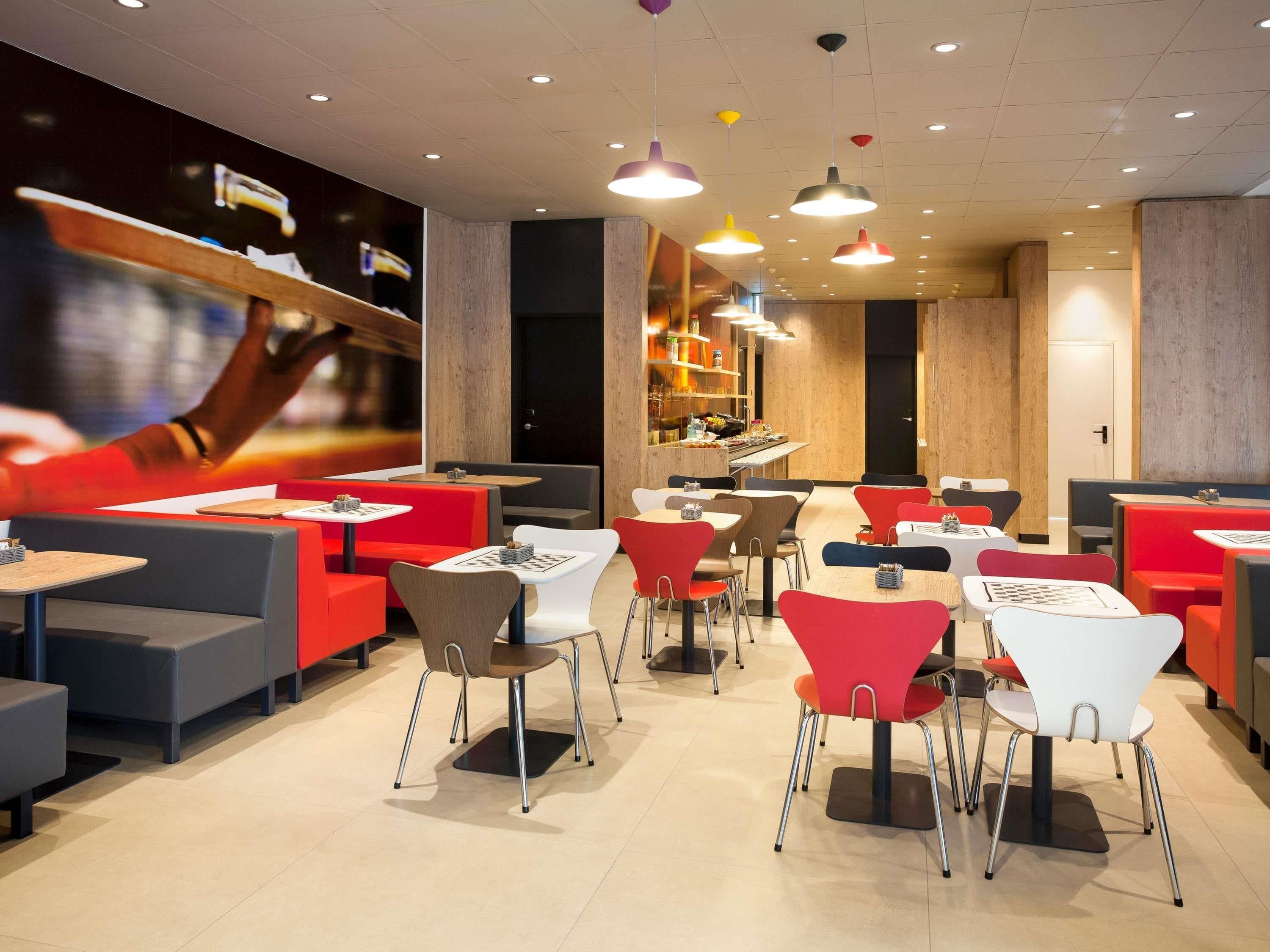 Un restaurante moderno con asientos rojos y blancos, varias mesas e iluminación colgante.