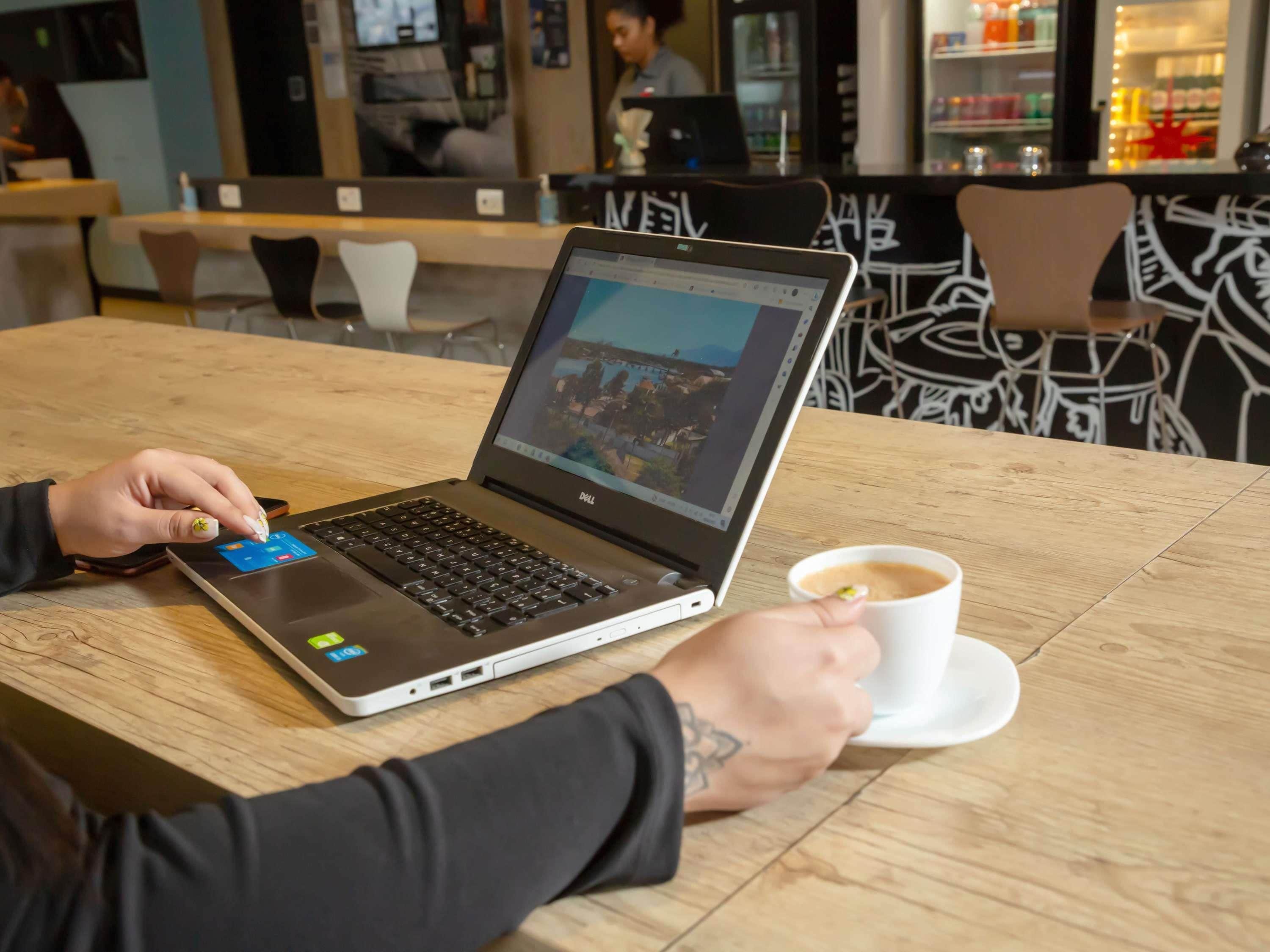 Una persona usando una computadora portátil en una mesa de madera en un café, con una taza de café.