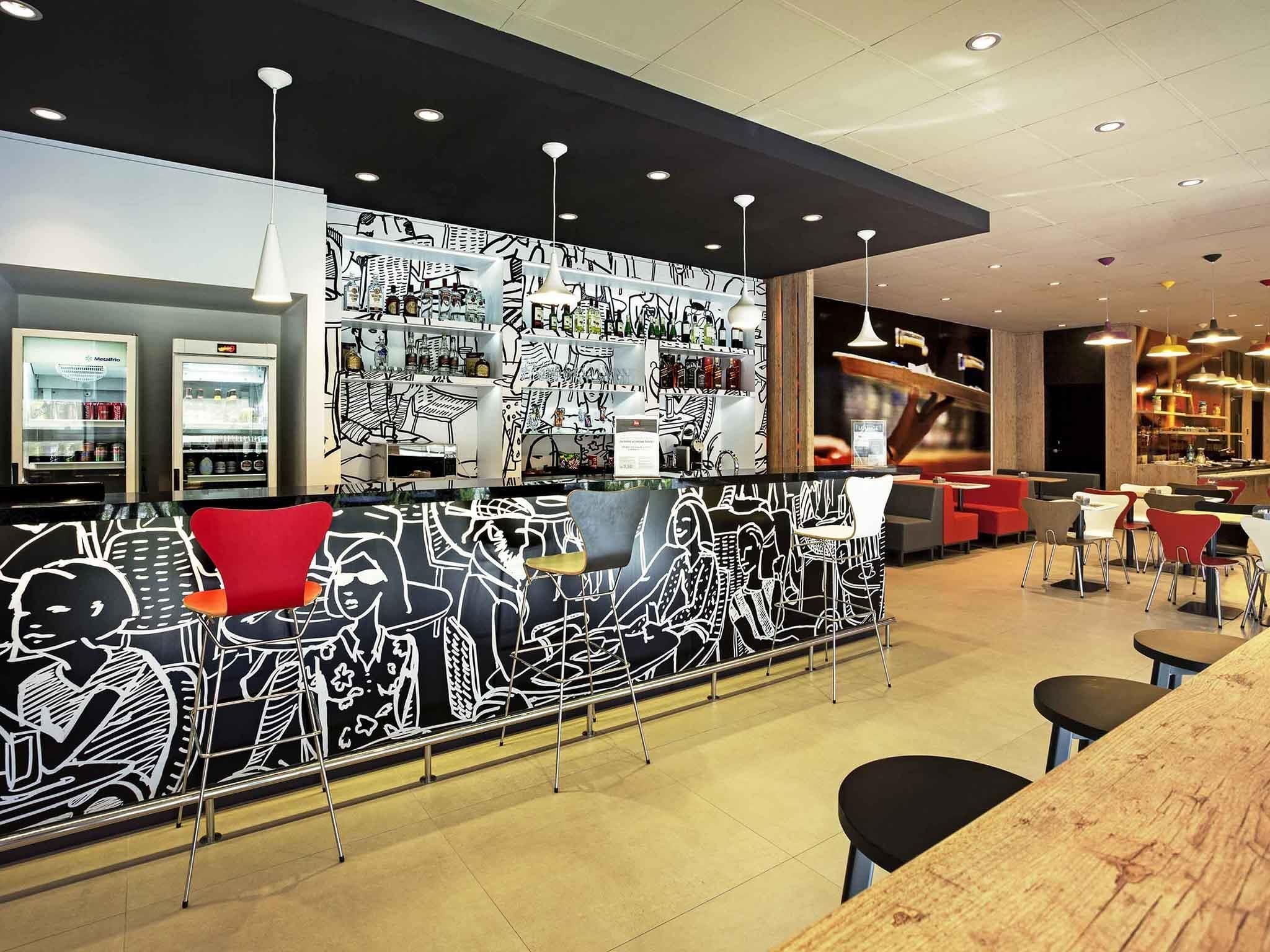 A modern bar area with a black and white mural, seating, and a counter with various items.