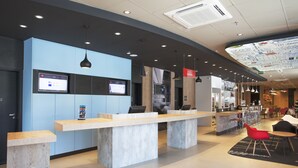 Una moderna zona de recepción con una pared azul, un mostrador alargado y una pantalla digital mostrando información.