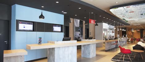 A modern reception area with a blue wall, a long reception desk, and a digital screen displaying information.