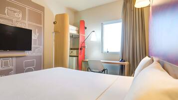 A hotel room with a bed, a desk, a chair, a TV, and a window with curtains.