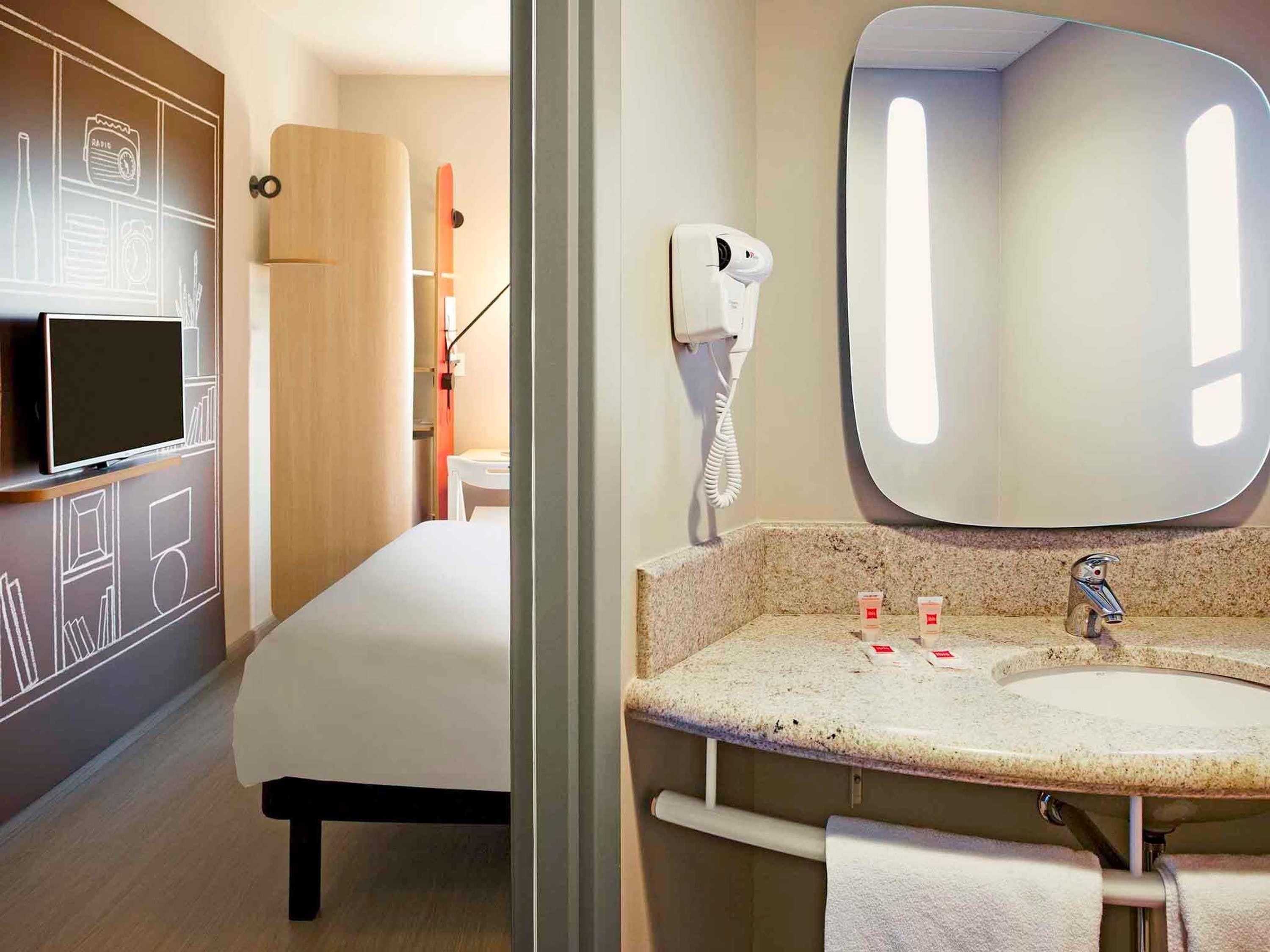 Hotelkamer met een bed, televisie, spiegel, wastafel en haardroger.