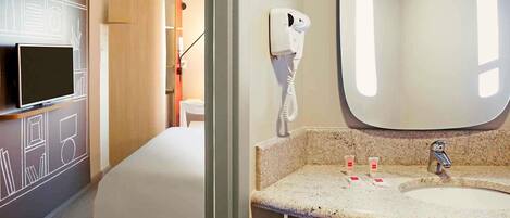A hotel room with a bed, a TV, a mirror, a sink, and a hairdryer.